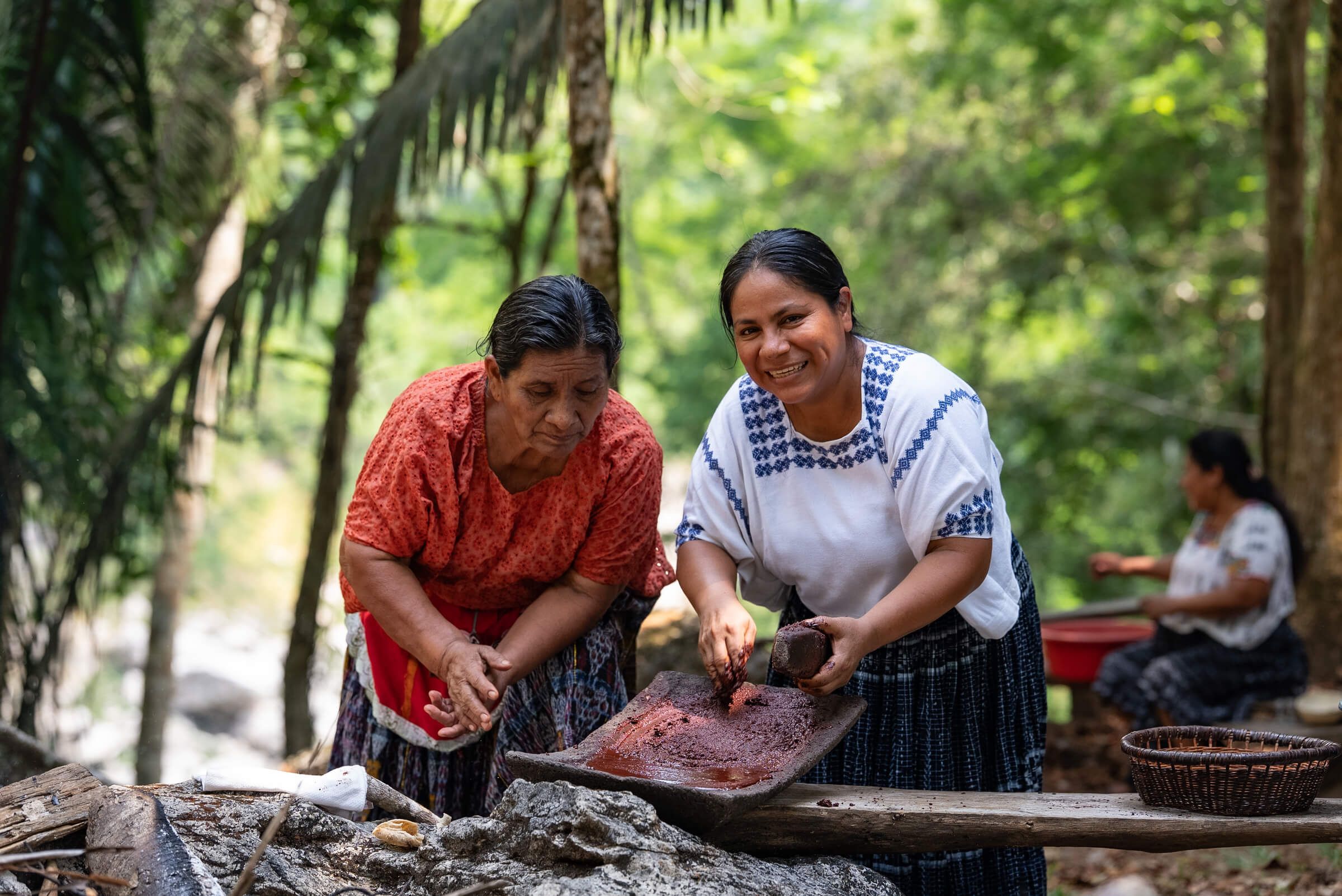 Zwei Frauen mahlen Kakao auf einem traditionellen Steinmetate in Guatemala